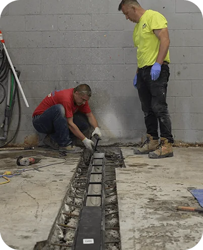 Two installers positioning a drain channel in a concrete floor trench