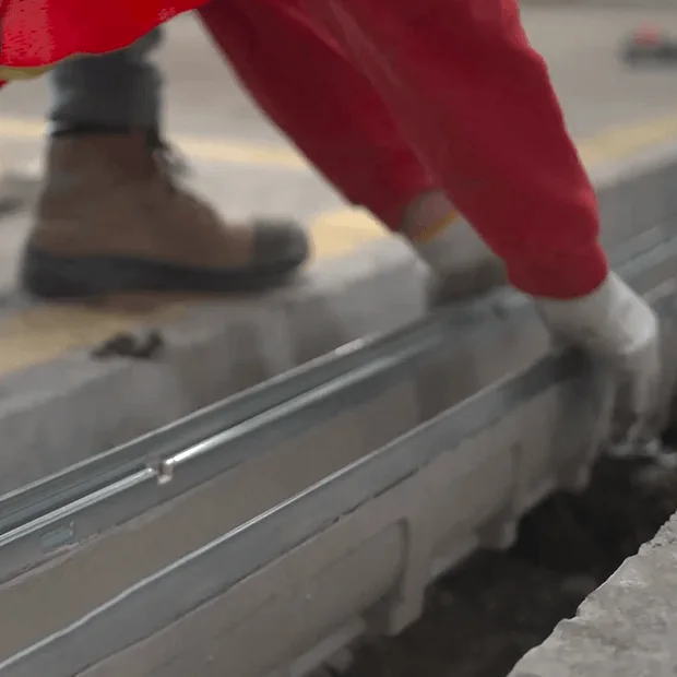 Gloved worker setting a metal drain channel into a floor trench